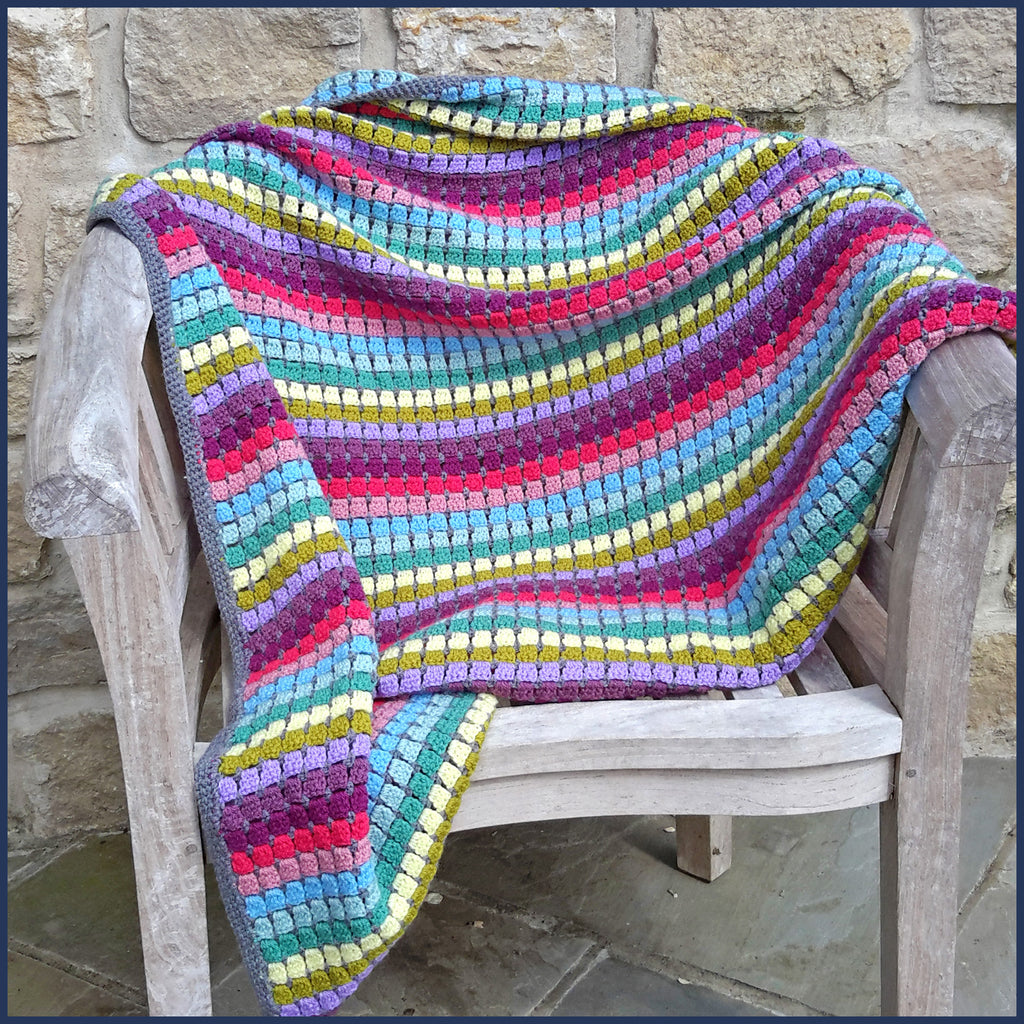 rainbow crochet blanket on a wooden chair