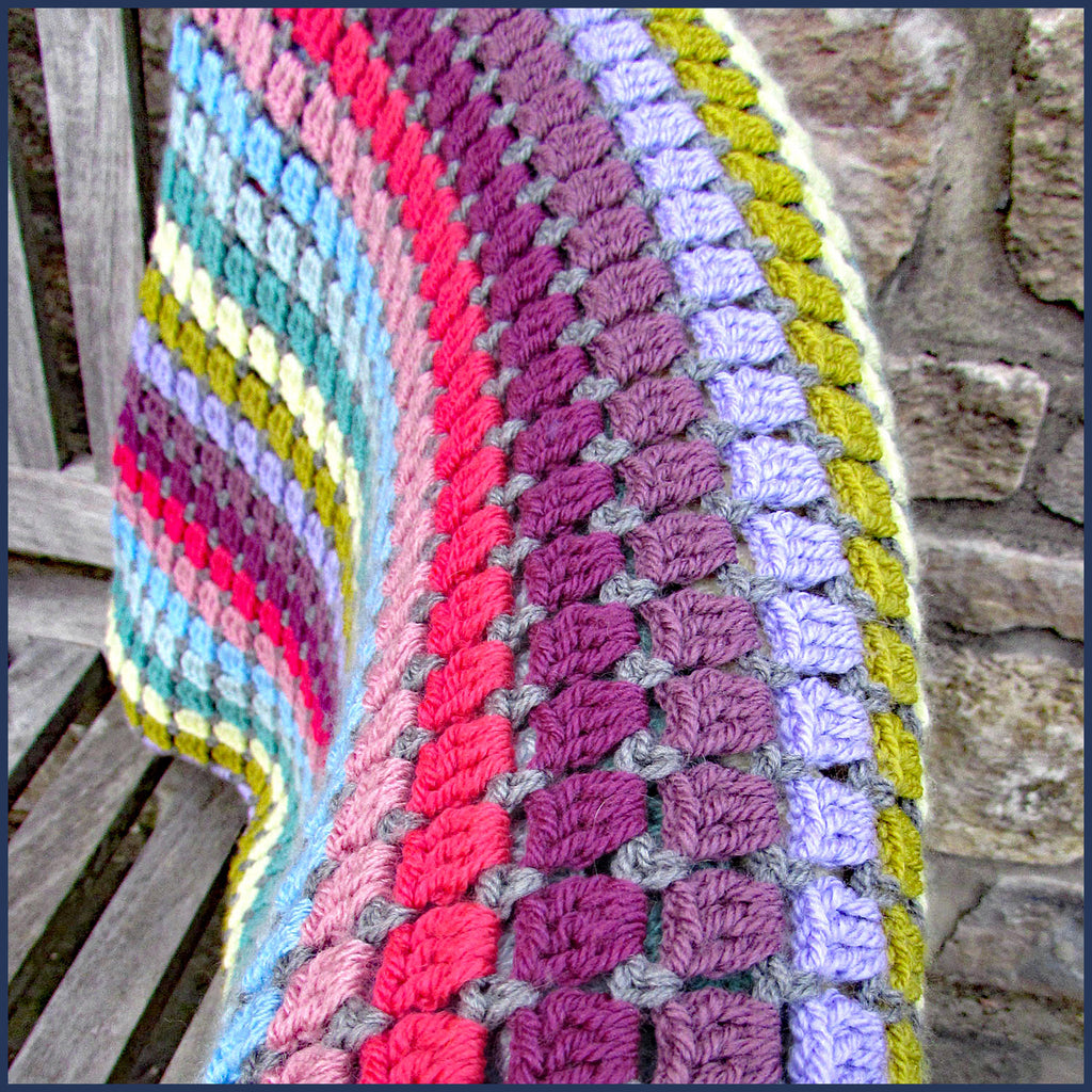 rainbow crochet blanket folded on a chair