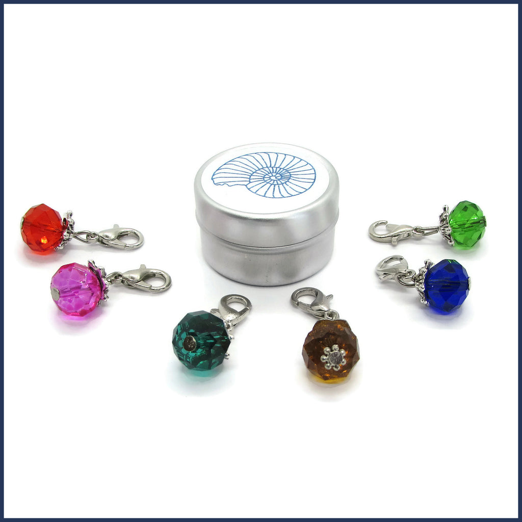 six colourful glass stitch markers with ammonite tin