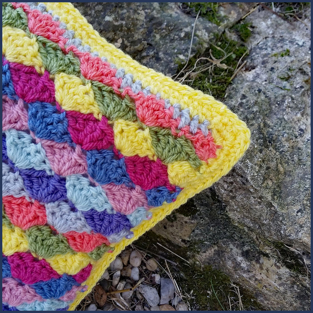 shell stitch crochet cushion against a stone wall