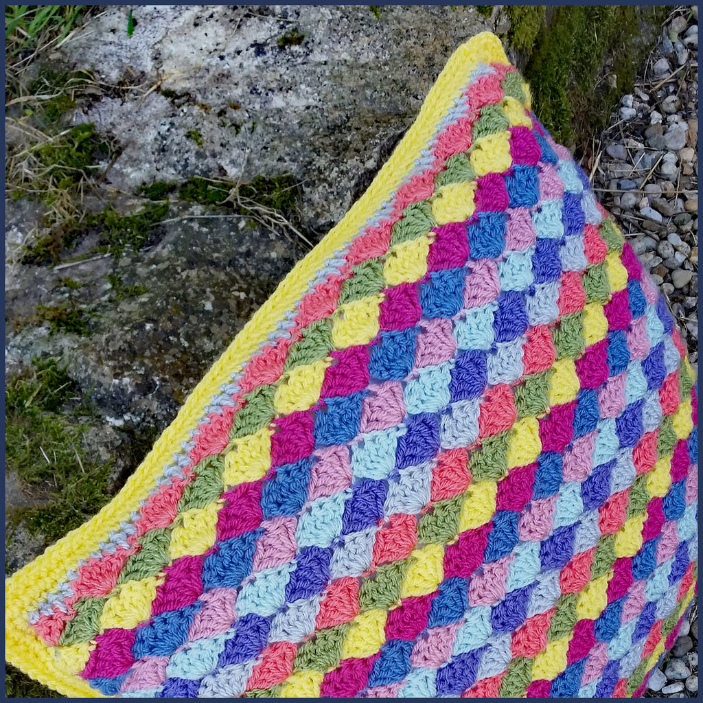 shell stitch crochet cushion against a stone wall