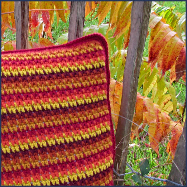 stripey crochet cushion against a wooden fence