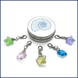 five glass star stitch markers with an ammonite tin
