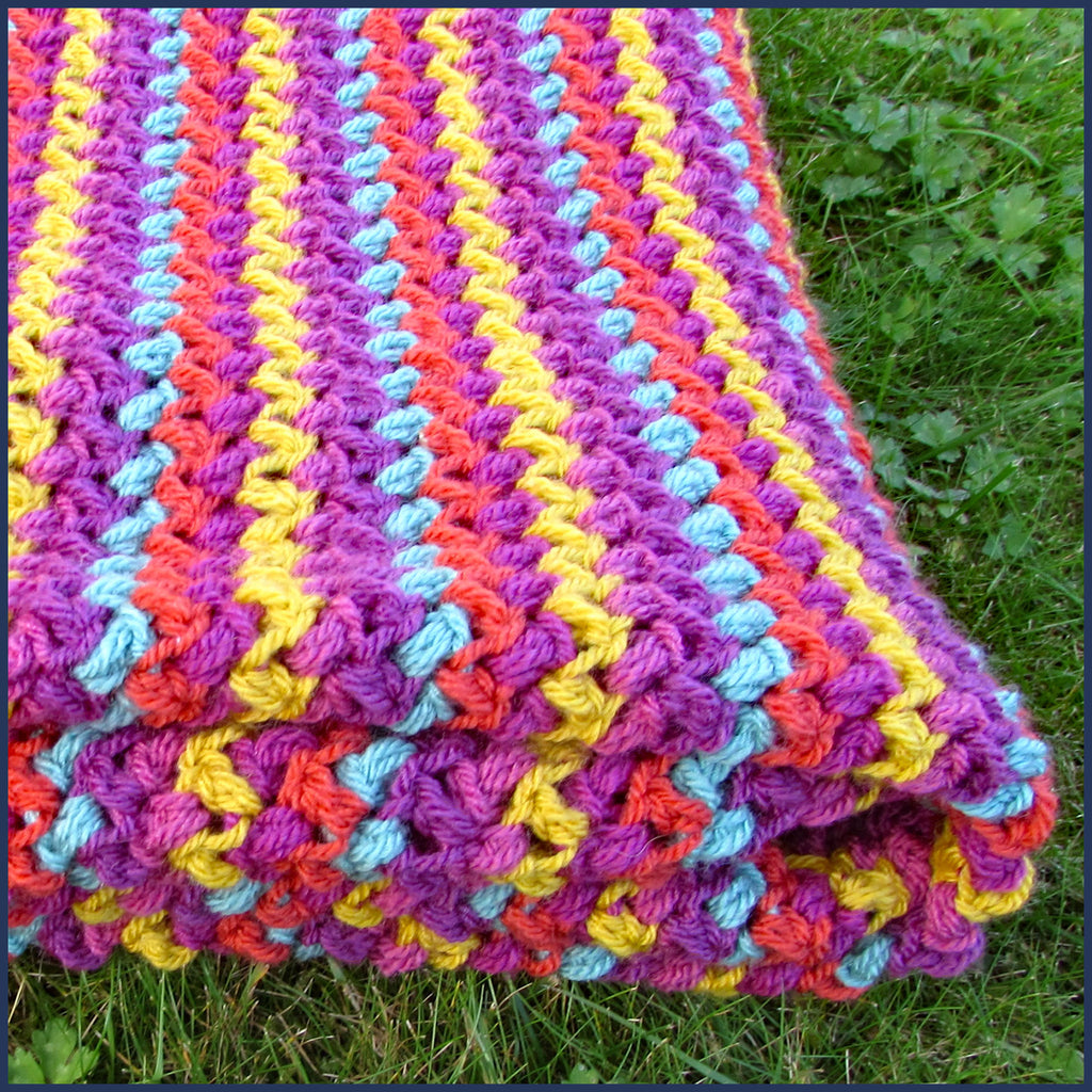 stripey crochet blanket folded on a lawn