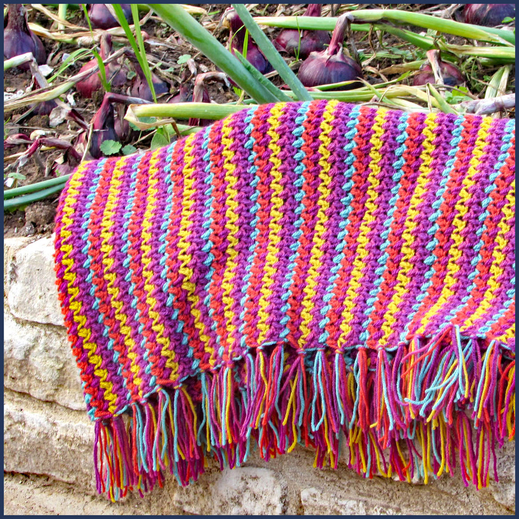 stripey crochet blanket on a veg patch with onions