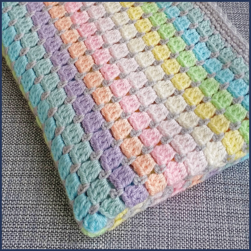 rainbow crochet baby blanket folded on a chair