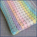rainbow crochet baby blanket folded on a chair