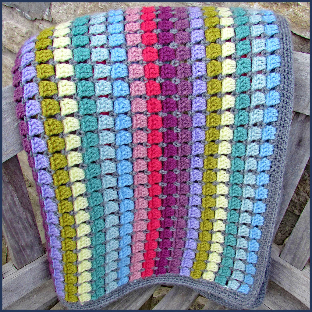 rainbow crochet blanket folded on a chair